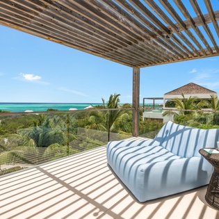 Unwind on your private terrace where striped shadows dance across plush seating, while turquoise waters shimmer beyond tropical palms.