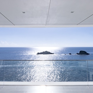 Stunning ocean views stretch endlessly before you from this covered terrace with glass railings and tropical palms.