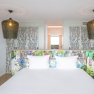 Drift into tropical dreams in your stylish bedroom with vibrant botanical headboard, elegant pendant lighting, and crisp white linens.