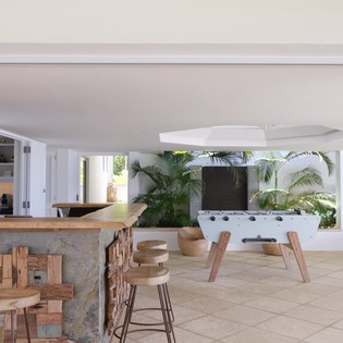 Gather with friends and family in this inviting covered entertainment space, complete with a foosball table, bar seating, and tropical greenery all around.