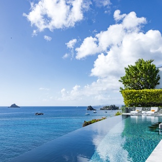 Stunning infinity pool overlooking pristine Caribbean waters with tropical landscaping and modern outdoor seating areas.