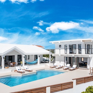 Modern villa with sparkling pool and bright blue sky, offering a luxurious retreat in a serene coastal setting.