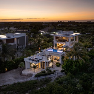 Modern luxury villa surrounded by tropical landscape captures golden sunset hues across the serene residential neighborhood.