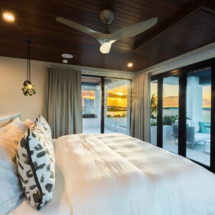 Wake up to golden sunsets and turquoise waters just beyond your door. This elegant bedroom opens onto a private terrace where the ocean stretches endlessly before you—pure coastal luxury.