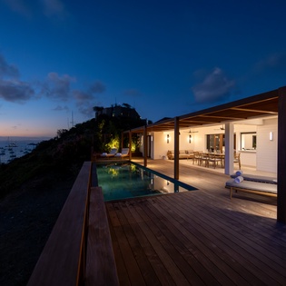 Luxury villa with infinity pool overlooking the ocean during twilight hours, featuring illuminated outdoor terrace and coastal views.