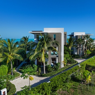 Modern beachfront villa surrounded by lush tropical gardens and swaying palms, just steps from pristine turquoise waters.