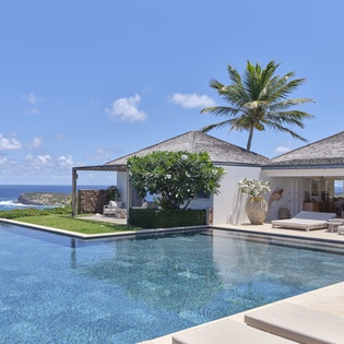 A stunning oceanfront villa with an infinity pool stretching toward endless blue waters. Swaying palms and open-air lounging areas frame your private tropical paradise.