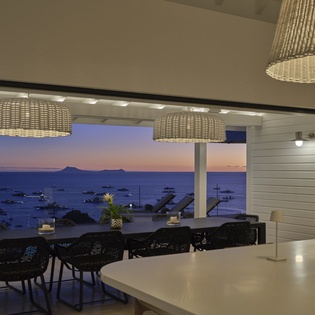 Your open-plan kitchen flows seamlessly to the dining terrace, where ocean views and twinkling harbor lights create the perfect dinner atmosphere.