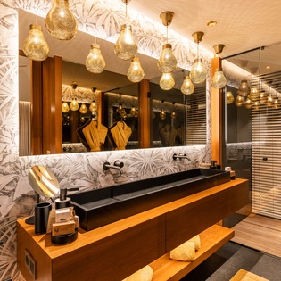 Step into your spa-like bathroom, where elegant pendant lights glow above sleek double vanities. Wrapped in warm wood and tropical-inspired tilework, this space invites you to unwind in style.