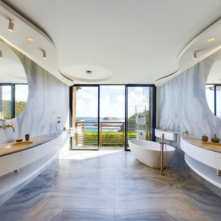 Step into your marble sanctuary where twin circular mirrors frame a freestanding tub overlooking stunning sea views through floor-to-ceiling windows.