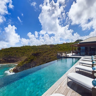 Infinity pool overlooking dramatic coastline with pristine turquoise waters and lush hillsides on a perfect sunny day.