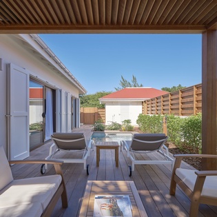 Unwind on your private terrace with modern seating, soothing hot tub, and beautiful garden views under peaceful blue skies.