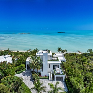 Stunning modern beachfront villa nestled among lush tropical foliage with pristine turquoise waters and small islands dotting the horizon, offering an idyllic island escape.