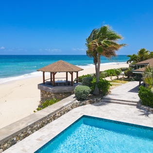 This beachfront property features a private pool, tropical gazebo, and direct access to pristine turquoise waters and soft white sand under endless blue skies.