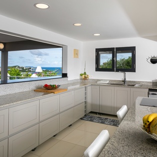 Your fully equipped kitchen opens to stunning sea views—perfect for preparing tropical breakfasts while soaking in the scenery through expansive windows and natural light.