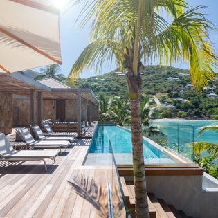 Tropical luxury awaits with this stunning infinity pool deck overlooking turquoise waters and lush hillsides.