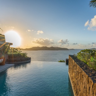 Spectacular infinity pool overlooks crystal-clear waters and distant islands as the golden sun sets over this tropical paradise.