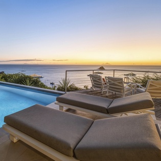 Private pool deck overlooking pristine ocean waters at golden hour, complete with comfortable loungers and dining area.