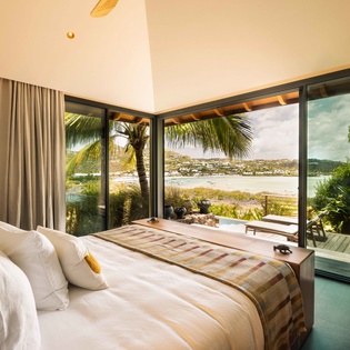 Wake up to stunning water and hillside views framed by floor-to-ceiling glass doors. Your serene bedroom opens directly onto a private terrace where tropical breezes and coastal beauty await.