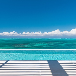 Crystal-clear infinity pool seamlessly blends with pristine turquoise ocean waters under brilliant blue skies.