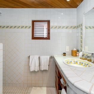 Relax in your bright, spacious bathroom featuring charming Mediterranean-inspired tilework, walk-in shower, handcrafted painted sink, and warm wood ceiling accents that create a welcoming retreat.