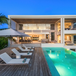 Modern luxury villa showcasing pristine swimming pool and elegant outdoor spaces beneath vibrant tropical skies.