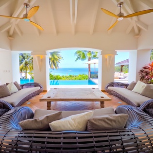 Unwind in your light-filled living space where curved lounges frame stunning views of the pool and ocean beyond. High vaulted ceilings, tropical breezes, and stylish touches create your perfect island escape.