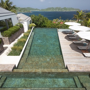 Stunning infinity pool overlooking turquoise Caribbean waters, surrounded by tropical palms and mountains.