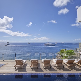 Waterfront pool deck with infinity edge, teak loungers, and panoramic ocean views featuring boats and islands.