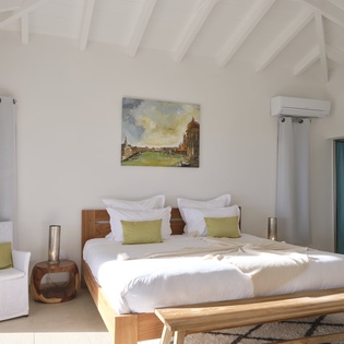 Unwind in your bright, airy bedroom featuring exposed beam ceilings, modern comfort, and crisp white linens with pops of green.