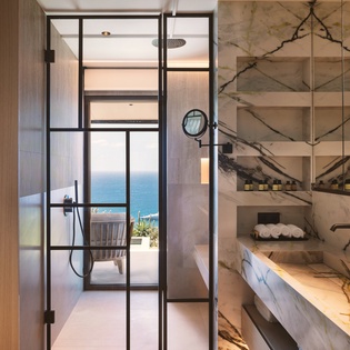 Step into your spa-like marble bathroom featuring a rainfall shower and stunning sea views through floor-to-ceiling windows.