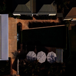 Aerial view showcasing the property's modern architecture with distinctive metal roofing and thoughtfully designed outdoor spaces featuring contemporary umbrella seating.