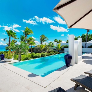 This pristine infinity pool overlooks lush gardens and turquoise coastal waters, framed by swaying palms and modern lounge chairs—perfect for soaking up sun-filled days.