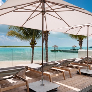 Luxurious beachfront deck with premium loungers and umbrellas overlooking pristine turquoise waters - your perfect tropical escape.