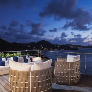 Elegant waterfront terrace overlooking tranquil bay at twilight, framed by rolling hills and distant lights. A refined outdoor retreat ideal for evening gatherings and serene contemplation.