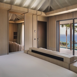 Wake up to stunning ocean views from your luxurious bedroom, where warm wood tones and floor-to-ceiling windows frame paradise perfectly.