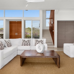 Sink into plush white furnishings in your bright, airy living space where floor-to-ceiling windows frame tropical views and warm wood accents create pure relaxation.