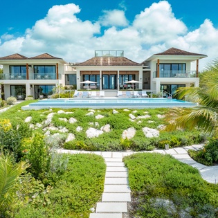 An impressive tropical estate featuring modern architecture, lush landscaped gardens, and a pristine pool set against a dramatic sky—a stunning vacation sanctuary.