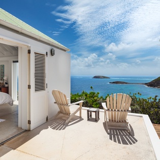 Step onto your private terrace where wooden chairs frame endless blue ocean vistas and distant islands—a serene outdoor retreat just beyond your bedroom door.