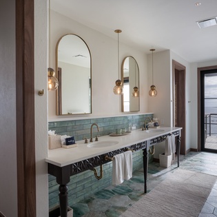 Your stunning bathroom features dual vanities with elegant brass fixtures and spectacular ocean views through floor-to-ceiling windows.