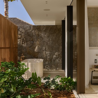 Your private sanctuary features a luxurious soaking tub surrounded by lush tropical plants and natural stone walls.