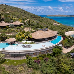 Stunning oceanfront villa with curved infinity pool overlooking turquoise Caribbean waters and pristine beaches.
