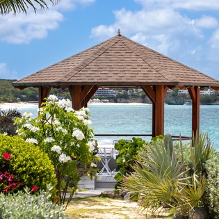 A tranquil seaside gazebo nestled among tropical gardens and blooming florals, overlooking crystal-clear waters and a scenic bay—perfect for morning coffee or sunset moments.