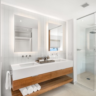 Step into your sleek spa-like bathroom featuring dual vanities, rainfall shower, and warm wood accents for your ultimate relaxation.