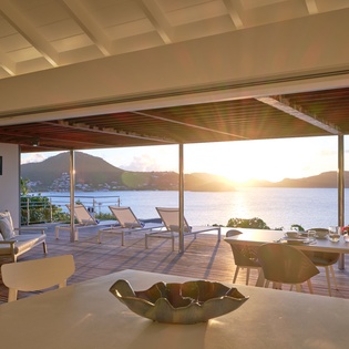 Stunning sea views frame your dining experience as golden sunset light pours through floor-to-ceiling windows onto elegant furnishings.