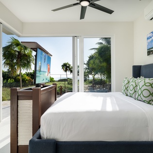 Wake up to tropical paradise through floor-to-ceiling windows, where soft breezes from your ceiling fan and ocean artwork complete your serene escape.