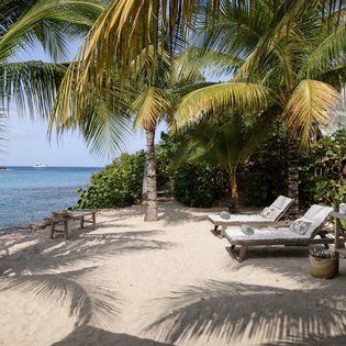Your private beachfront paradise awaits with loungers perfectly positioned under swaying palms, where crystal-clear waters and soft sand create your ultimate tropical escape.
