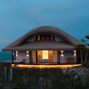 Stunning thatched-roof villa overlooking turquoise waters at twilight, where tropical luxury meets serene oceanfront tranquility.