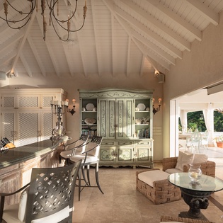 Step into your own island retreat, where vaulted white-beamed ceilings soar above elegant seating and a vintage-style hutch. French doors frame tropical greenery and your private outdoor terrace beyond.