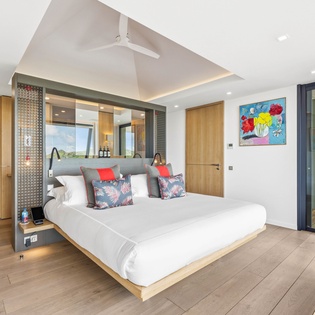 Step into your spacious modern bedroom where warm wood meets cool stone floors. Colorful art brightens white walls while your private balcony awaits morning coffee moments.